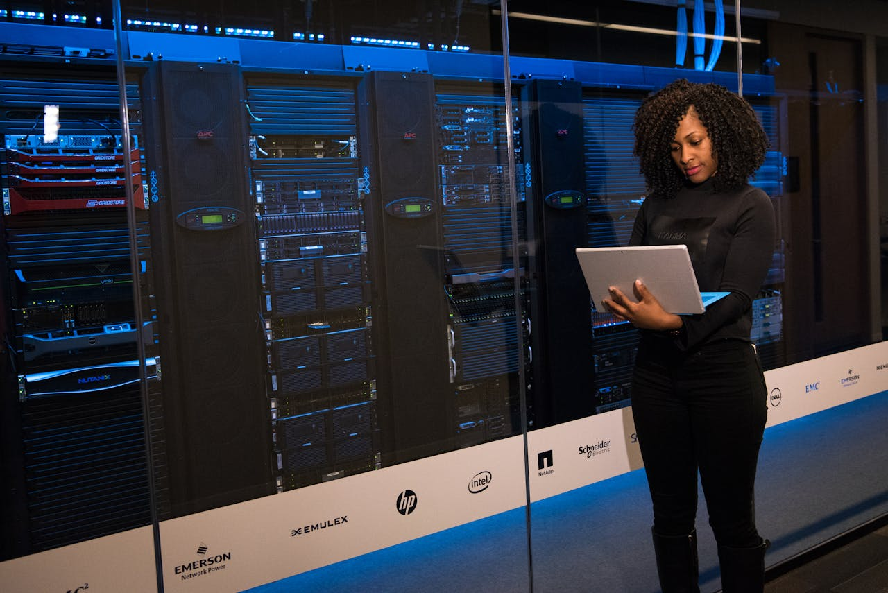 why-choose-us A female engineer using a laptop while monitoring data servers in a modern server room.