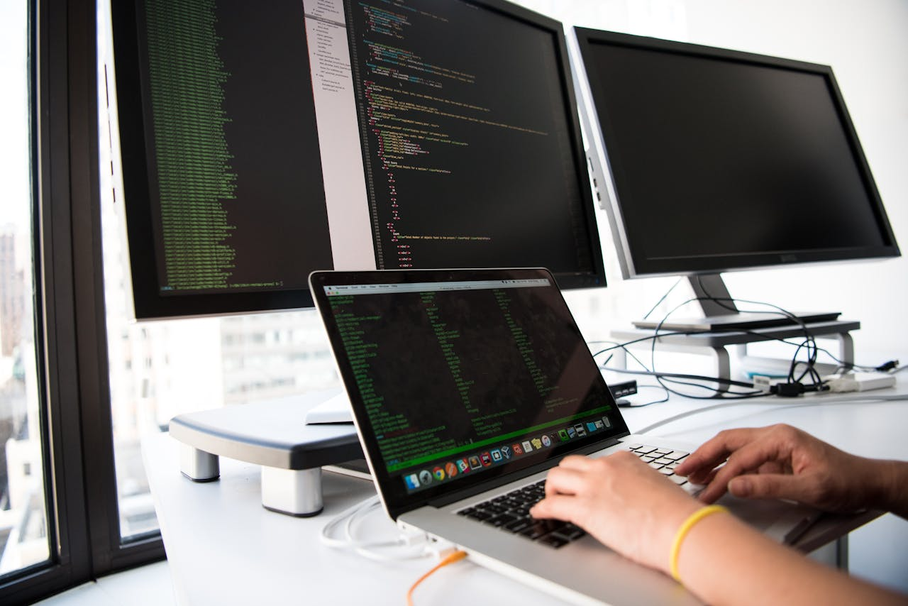journey A developer writes code on a laptop in front of multiple monitors in an office setting.